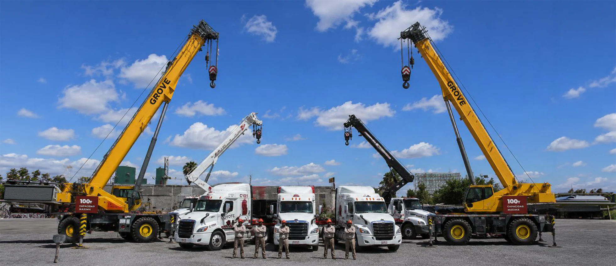 Flota completa de Transportes Coyote en patio: dos grúas Grove de 100 toneladas con las plumas elevadas, tres tractocamiones y el equipo de operadores